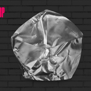 May include: A silver, crumpled, metallic object with a geometric shape, resembling a star or a flower, against a black brick wall background.