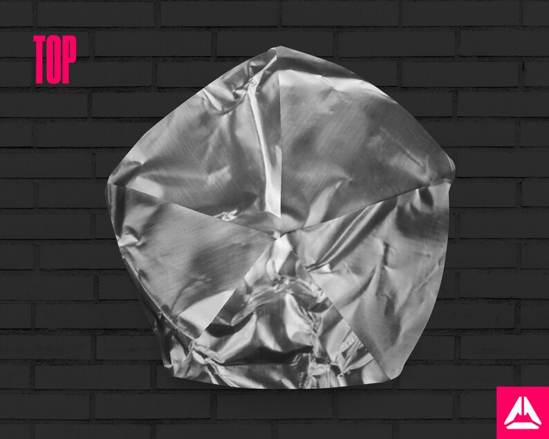 May include: A silver, crumpled, metallic object with a geometric shape, resembling a star or a flower, against a black brick wall background.