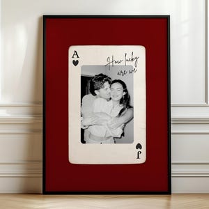 May include: A framed black and white photograph of a couple embracing, set against a red background. The photo is shaped like a playing card, with the Ace of Hearts and Ace of Spades symbols visible. The text "How lucky are we" is written on the card.