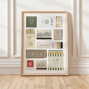 May include: A framed collection of vintage matchboxes. The matchboxes feature various designs, including cocktail glasses, tennis rackets, and travel destinations. The color palette includes green, beige, and white, with gold accents. The frame is a light wood color.