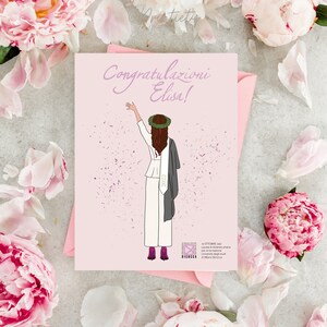 Può includere: Un biglietto rosa con il testo "Congratulazioni Elisa!" e un'illustrazione a cartone animato di una donna con una toga da laurea bianca e un cappello, che lancia il suo cappello in aria. Lo sfondo è pieno di coriandoli.