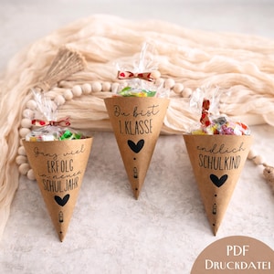 May include: Three brown paper cone-shaped containers filled with sweets, each with a different German phrase in black script and a black heart. The cones are tied with clear cellophane and decorative bows. The text includes "1. Klasse" and "endlich SCHULKIND".