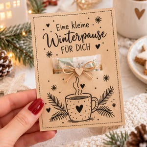 Könnte beinhalten: Eine rechteckige Karte aus Kraftpapier mit dem schwarzen Aufdruck "Eine kleine Winterpause FÜR DICH" über einer Grafik einer dampfenden Tasse mit Herz. Ein kleines durchsichtiges Tütchen ist mit einer Juteschleife und einem Holzherz befestigt.