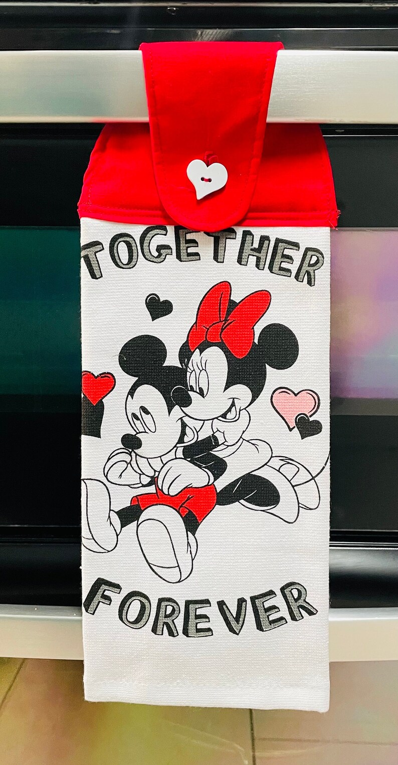 Puede incluir: Toalla de cocina blanca con un lazo rojo para colgar. La toalla presenta una ilustraci&oacute;n en blanco y negro de Mickey Mouse y Minnie Mouse con el texto "Together Forever".