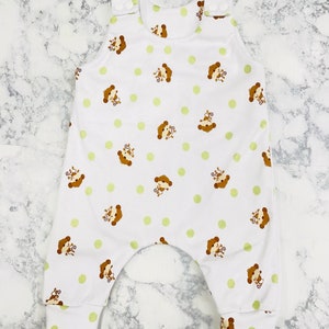 May include: White baby onesie with a green and brown monkey print. The onesie has a sleeveless design and snaps at the shoulders.