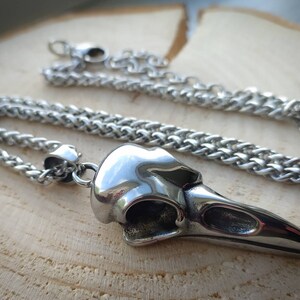 May include: A silver chain necklace with a detailed crow skull pendant. The pendant is made of metal and has a realistic design.