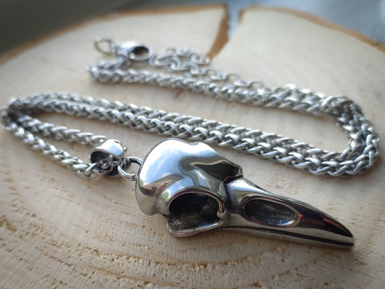 May include: A silver chain necklace with a detailed crow skull pendant. The pendant is made of metal and has a realistic design.