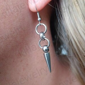 May include: Silver spike earrings with a chain of small silver rings. The earrings are hanging from a person's ear.