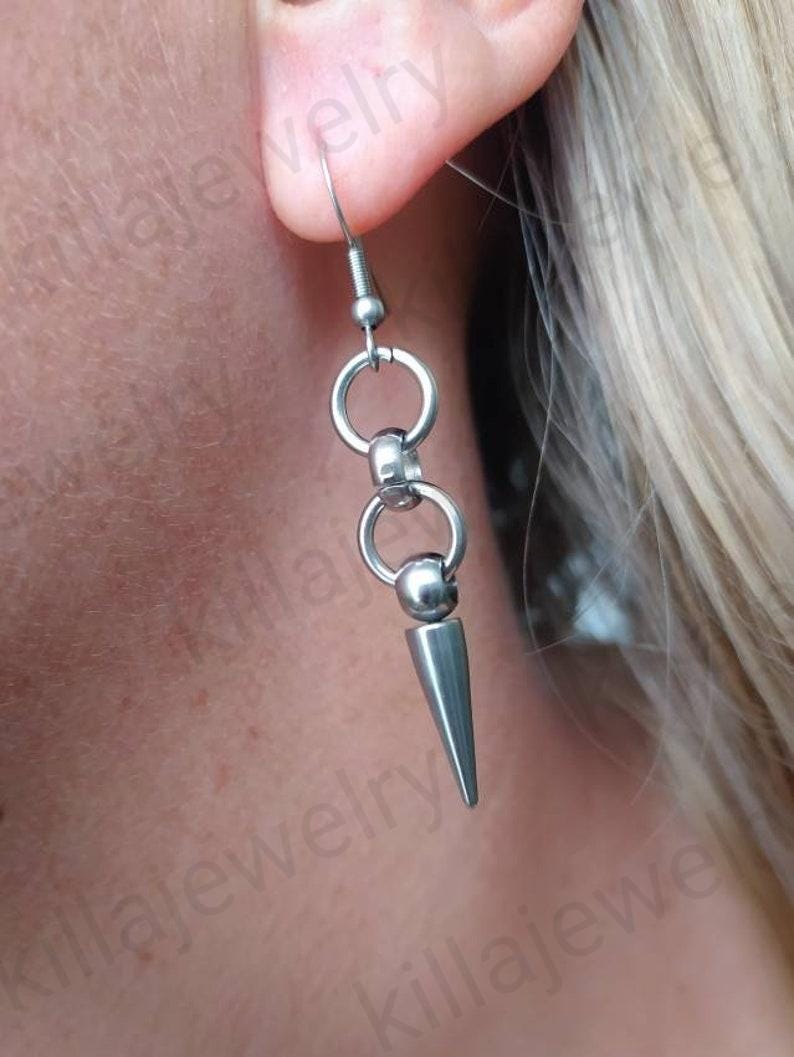 May include: Silver spike earrings with a chain of small silver rings. The earrings are hanging from a person's ear.