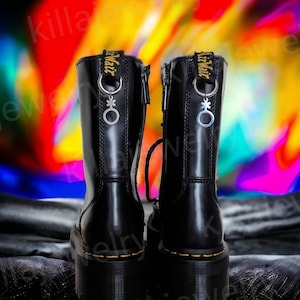 May include: A pair of black leather boots with a thick platform sole and a zipper on the side. The boots have a silver charm attached to the laces, featuring a gender symbol.