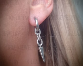 May include: A silver earring with a small, pointed spike hanging from a chain. The earring is worn in the upper lobe of a person's ear.