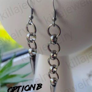 May include: A pair of silver earrings with a chain and a pointed tip. The earrings are hanging from a white surface. The text "OPTION B" is visible in the image.