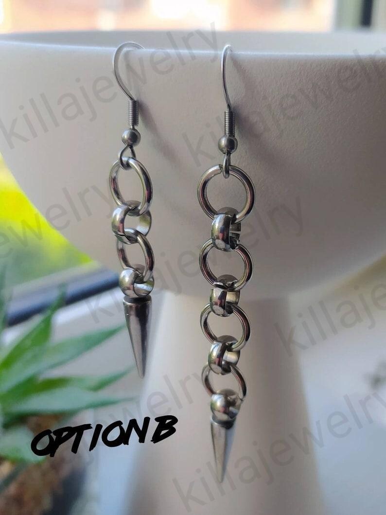 May include: A pair of silver earrings with a chain and a pointed tip. The earrings are hanging from a white surface. The text "OPTION B" is visible in the image.