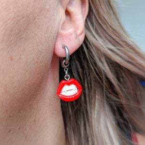 May include: Silver hoop earrings with a red and white dangling charm of a mouth with fangs.