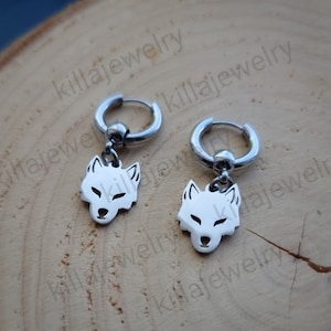 May include: A pair of silver hoop earrings with a wolf head charm hanging from each hoop.