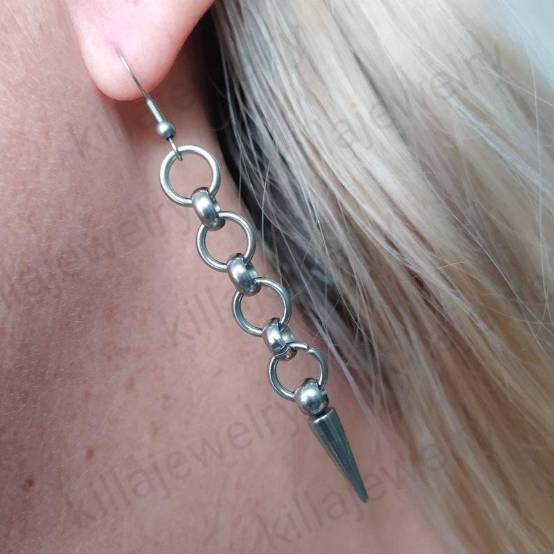 May include: Silver chain earrings with a pointed tip. The chain is made of small, round links.