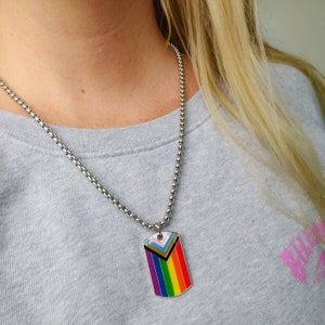 May include: A silver chain necklace with a silver dog tag pendant featuring a rainbow pride flag design.
