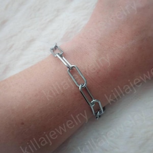 May include: A silver chain bracelet with oval links. The bracelet is on a person's wrist.