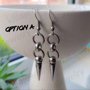 May include: A pair of silver earrings with a spike design. The earrings feature two connected rings and a small ball at the top of the spike.