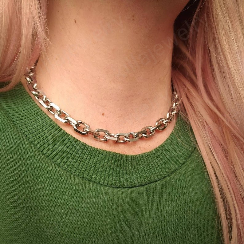 Puede incluir: Un collar de cadena plateado con un dise&ntilde;o de eslabones gruesos. El collar lo lleva una persona con el pelo rosa y una camisa verde.