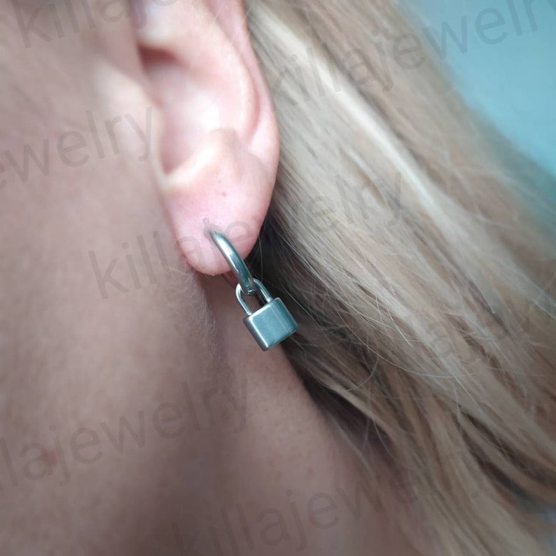 May include: Silver hoop earrings with a small padlock charm hanging from each hoop.