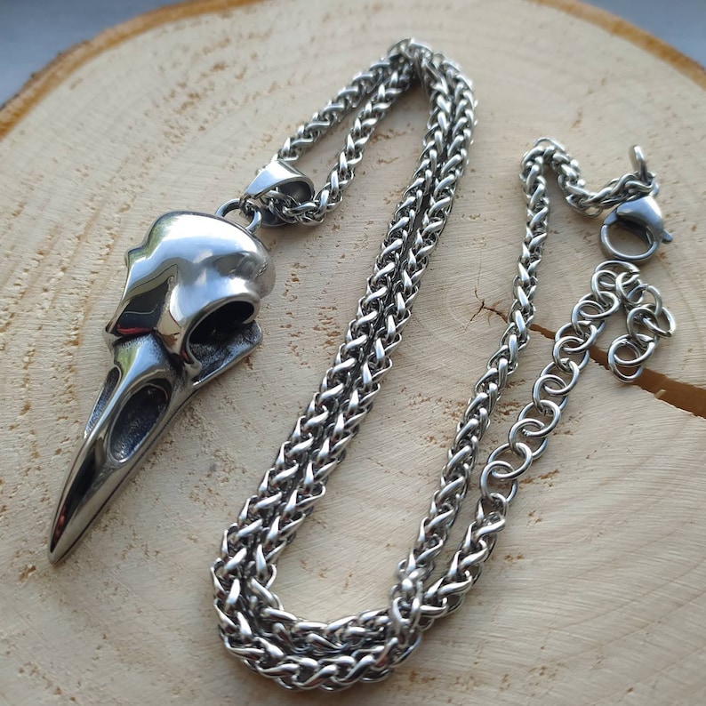 May include: A silver chain necklace with a detailed bird skull pendant. The chain is a braided style and has a lobster clasp.