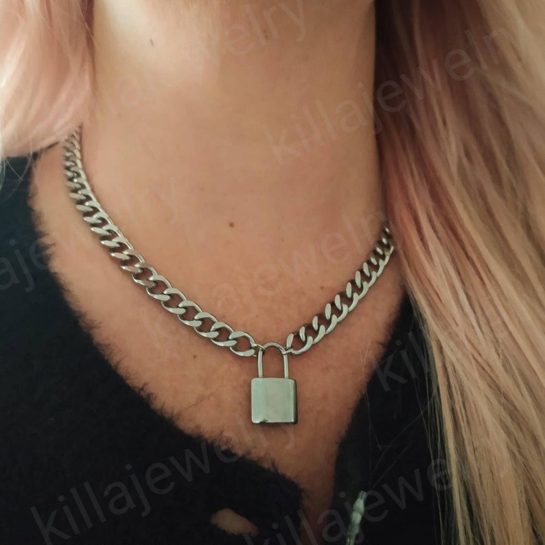 K&ouml;nnte beinhalten: Eine silberne Kettenkette mit einem Schlossanh&auml;nger. Die Kette ist dick und hat ein Gliederketten-Design.