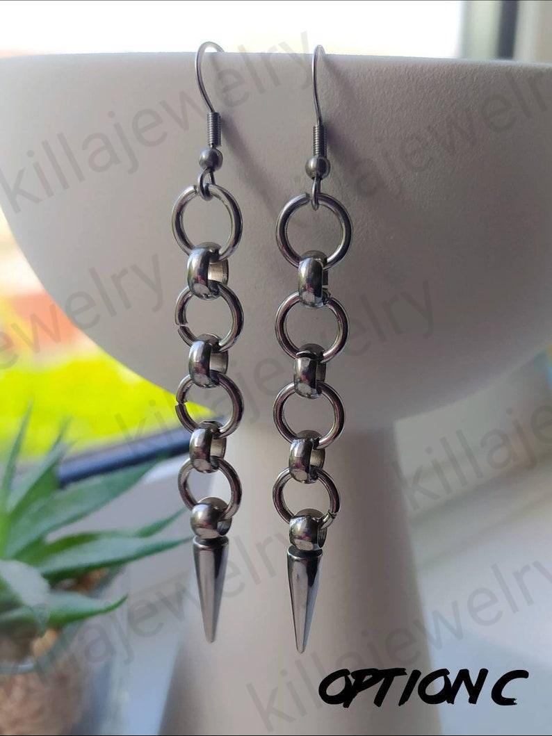 May include: A pair of silver earrings with a chain link design and a pointed spike at the bottom. The earrings are hanging from a white surface.