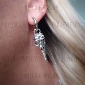 May include: Silver skull earring with a hoop. The skull has a detailed design and a long beak.