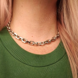 Puede incluir: Un collar de cadena plateado con un dise&ntilde;o de eslabones gruesos. El collar lo lleva una persona con el pelo rubio y una camisa verde.