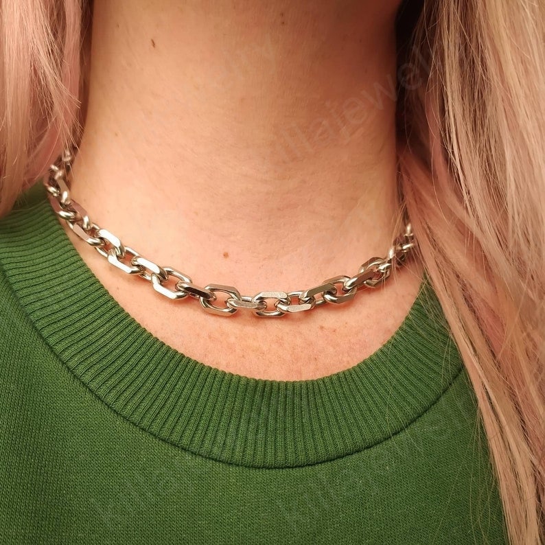 Puede incluir: Un collar de cadena plateado con un dise&ntilde;o de eslabones gruesos. El collar lo lleva una persona con el pelo rubio y una camisa verde.