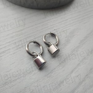 May include: A pair of silver hoop earrings with a padlock charm hanging from each hoop.