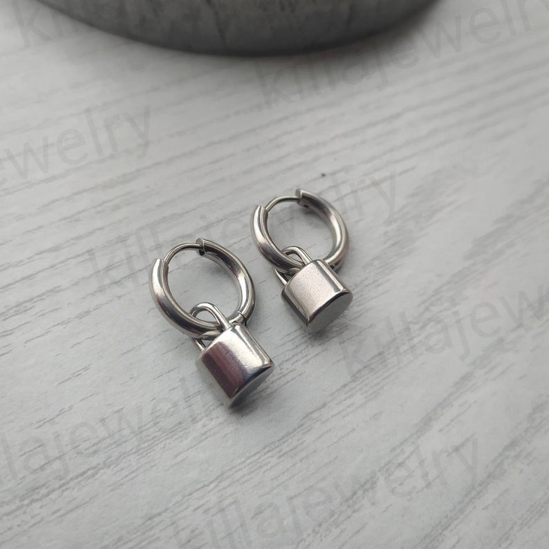 May include: A pair of silver hoop earrings with a padlock charm hanging from each hoop.