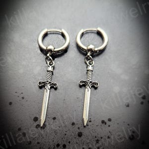 May include: A pair of silver hoop earrings with a sword charm hanging from each hoop. The swords have a detailed design and are pointed.