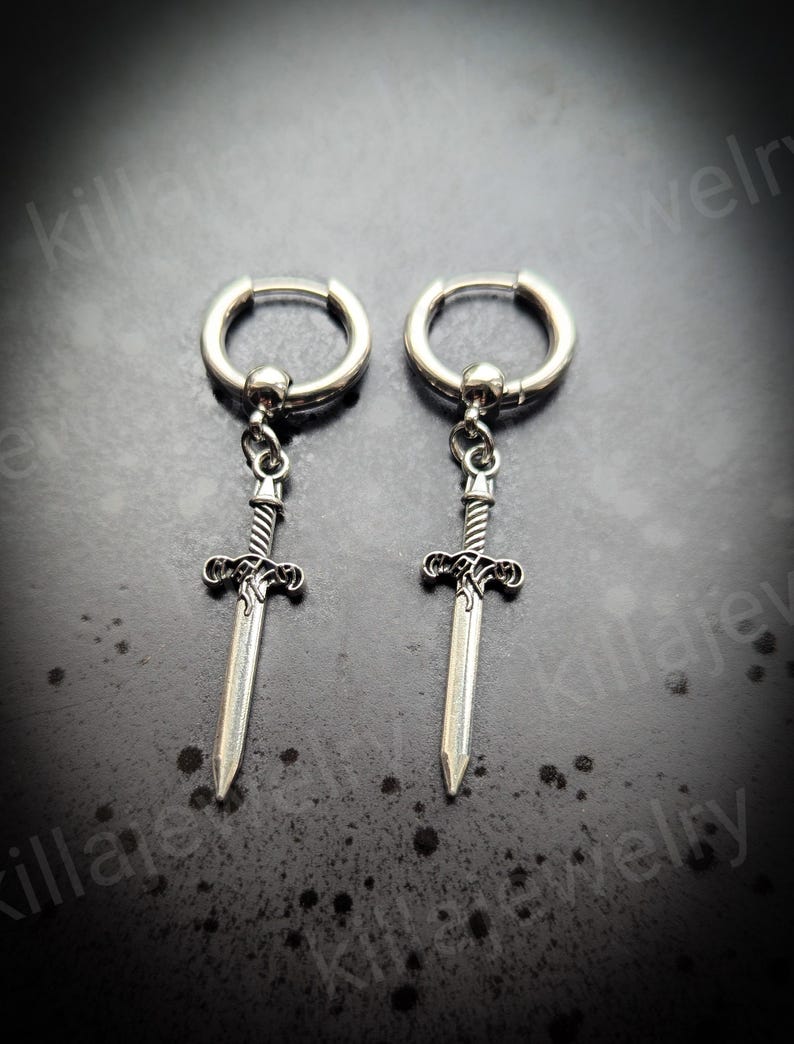 May include: A pair of silver hoop earrings with a sword charm hanging from each hoop. The swords have a detailed design and are pointed.