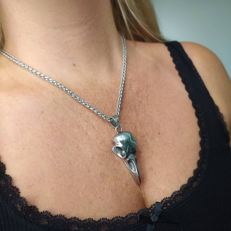 May include: A silver chain necklace with a detailed silver bird skull pendant. The pendant is shaped like a bird's skull with a long beak.