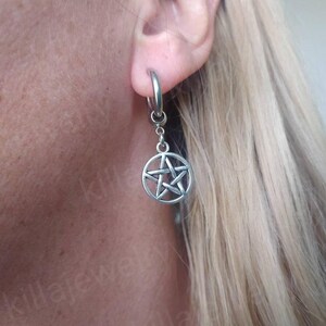 Peut inclure: Boucle d'oreille argent&eacute;e avec un pendentif pentagramme. La boucle d'oreille est de type cr&eacute;ole, avec une attache circulaire pour l'oreille. Le pendentif est une &eacute;toile &agrave; cinq branches dans un cercle. La boucle d'oreille est port&eacute;e &agrave; l'oreille.