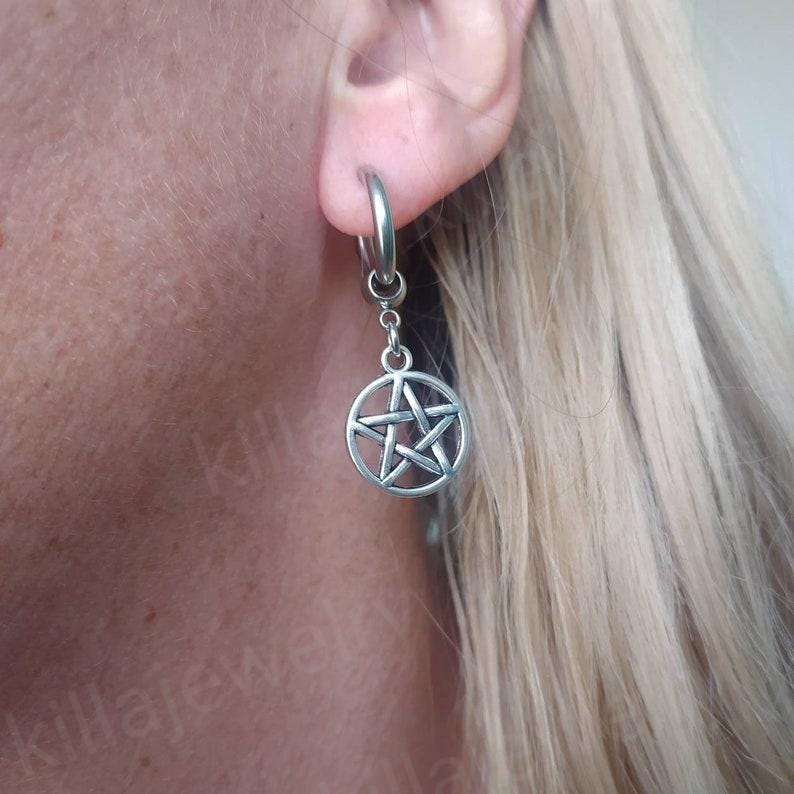 Peut inclure: Boucle d'oreille argent&eacute;e avec un pendentif pentagramme. La boucle d'oreille est de type cr&eacute;ole, avec une attache circulaire pour l'oreille. Le pendentif est une &eacute;toile &agrave; cinq branches dans un cercle. La boucle d'oreille est port&eacute;e &agrave; l'oreille.