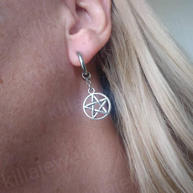 Peut inclure: Boucle d'oreille argent&eacute;e avec un pendentif en forme de pentagramme. La boucle d'oreille est attach&eacute;e &agrave; un anneau ins&eacute;r&eacute; dans l'oreille. Le pendentif est une &eacute;toile &agrave; cinq branches dans un cercle. Fond de cheveux blonds et de peau.