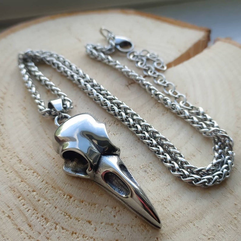 May include: A silver necklace with a detailed crow skull pendant. The chain is a braided rope style.