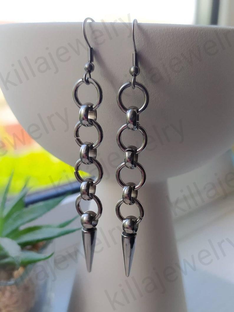May include: A pair of silver earrings with a chain link design and a pointed spike at the bottom.