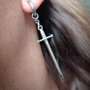 May include: Silver sword dangle earring with a hoop. The sword is attached to a chain that hangs from the hoop.