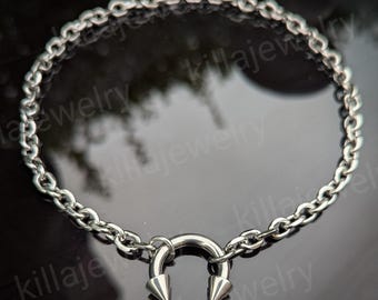 May include: A silver chain necklace with a silver horseshoe pendant with two pointed ends. The necklace is on a reflective surface.