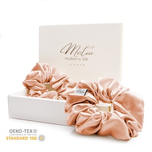 May include: Two peach-coloured silk scrunchies in a white box with the text "Morton Mulberry Silk London" on the lid. The box also has the Oeko-Tex Standard 100 logo.