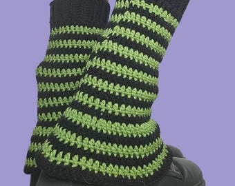 May include: Crocheted leg warmers in black and green stripes. The leg warmers are worn over black platform shoes and patterned tights. The leg warmers are a cozy accessory for colder weather or a unique fashion statement.