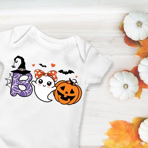 May include: White baby onesie with a Halloween-themed graphic. The design includes the word "BOO" with a witch hat, spiderweb, and ghost, along with a pumpkin and bats. The onesie is decorated with hearts and a polka-dot bow.