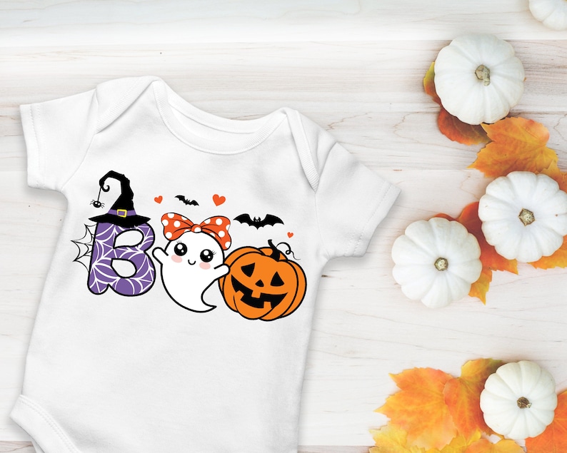 May include: White baby onesie with a Halloween-themed graphic. The design includes the word "BOO" with a witch hat, spiderweb, and ghost, along with a pumpkin and bats. The onesie is decorated with hearts and a polka-dot bow.