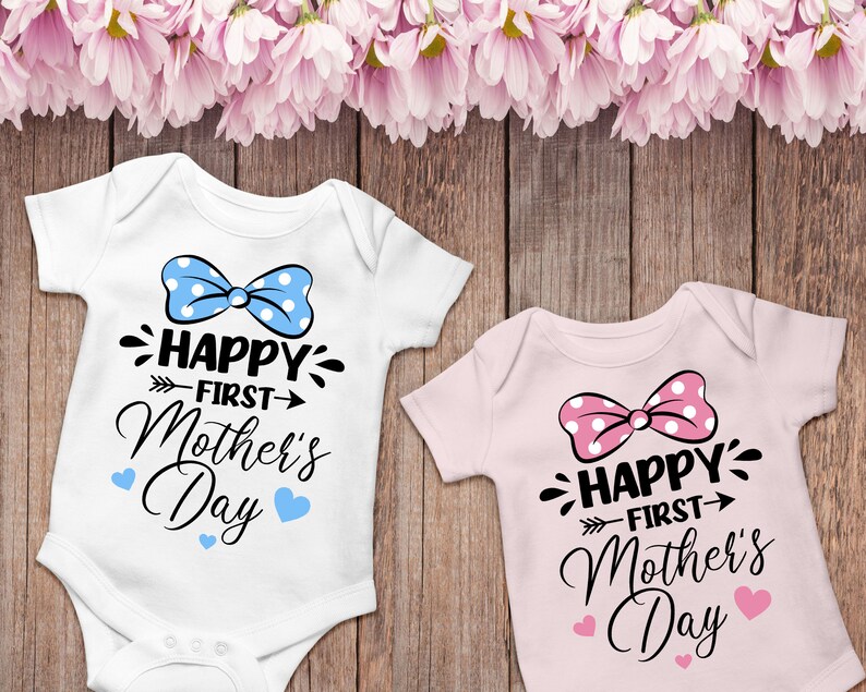 Peut inclure: Deux bodies blancs pour b&eacute;b&eacute; avec un n&oelig;ud et le texte "Happy First Mother's Day". Un body a un n&oelig;ud bleu et des c&oelig;urs bleus, l'autre a un n&oelig;ud rose et des c&oelig;urs roses.
