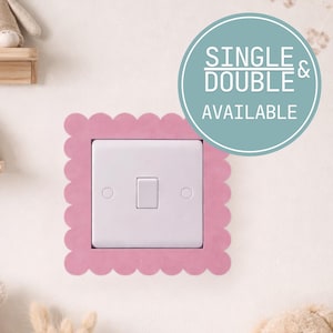 May include: A white light switch set within a pink, scalloped frame. The text "SINGLE & DOUBLE AVAILABLE" is in a teal circle. The image is of a nursery or children's room.