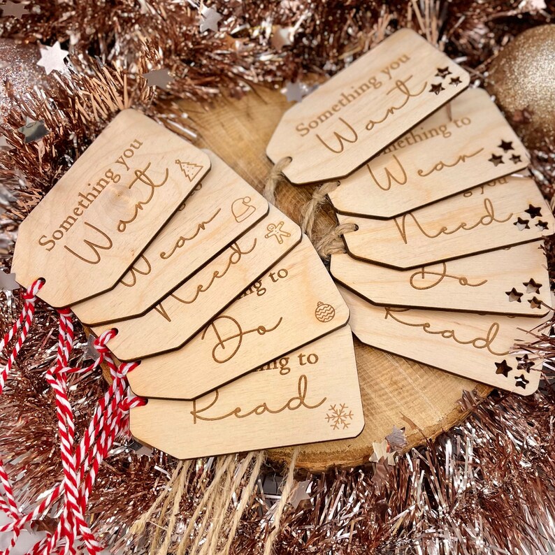 May include: A set of six wooden gift tags with the words "Something you Want", "Something you Wear", "Something you Need", "Something to Do", "Something to Read", and "Something you Need" written on them. The tags are decorated with stars and other festive designs.